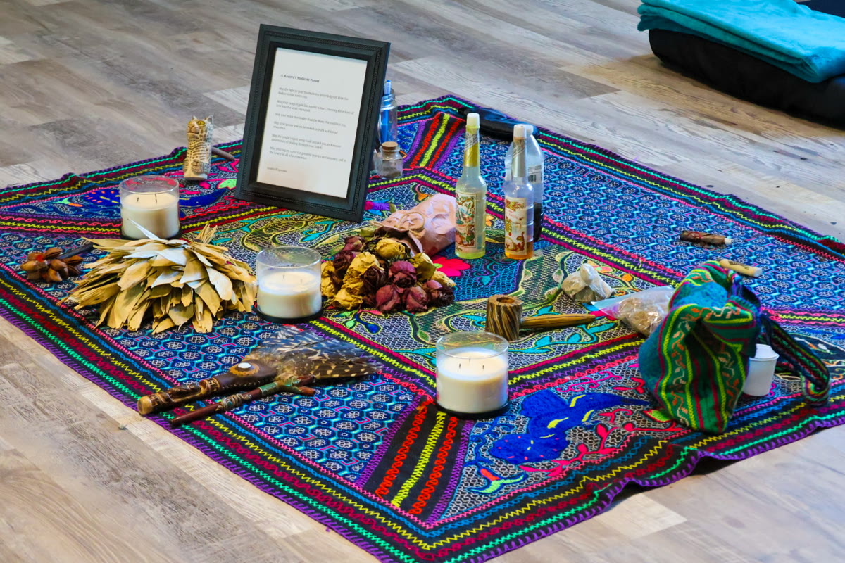 Close view of the altar: candles, florida water, and a framed prayer on a Shipibo textile
