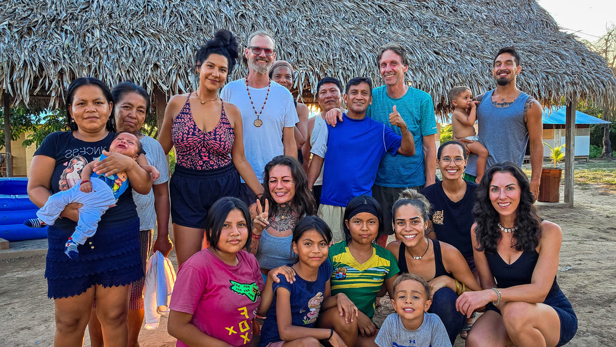 Guests gathered with a Shipibo family beneath a palm-thatch roof in the Peruvian Amazon, warm evening light
